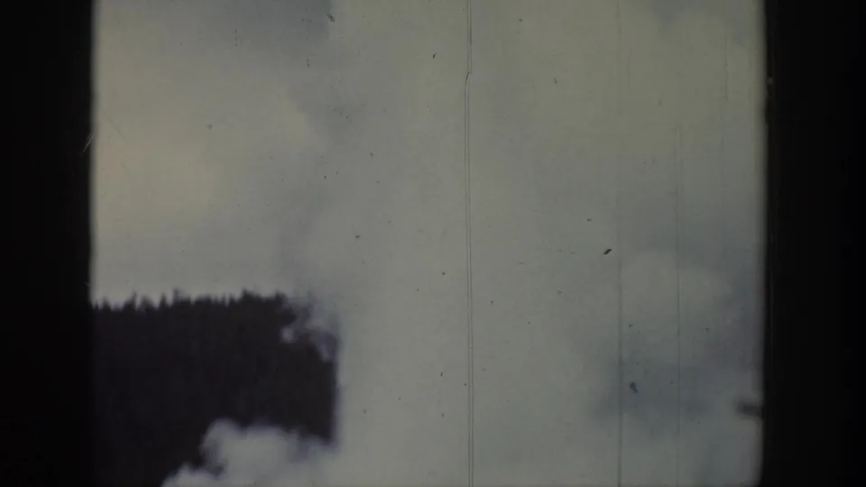 1939 Wyoming frame showing a broad geyser steam cloud filling the view above a dark forest edge.