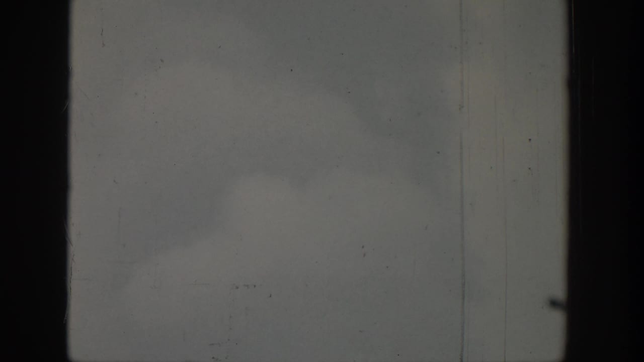 1939 8mm frame with a dark vertical edge, pale overcast texture, scratches, dust, and no visible people or brands.
