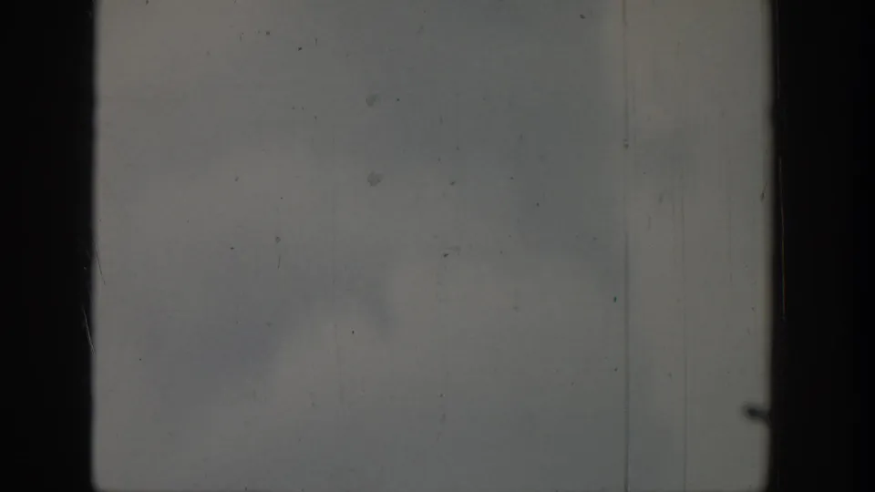 1939 8mm frame showing a dark vertical band, pale gray-blue tones, film scratches, dust, and indistinct storm texture.