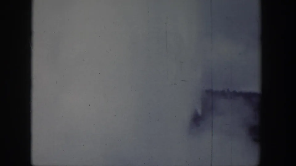 1939 8mm frame with a dark side edge, pale scratched surface, horizontal exposure shift, and a blurred dark shape near the lower area.