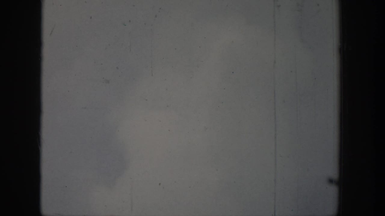1939 Wyoming 8mm frame showing a faint geyser spray or steam plume rising against a cloudy sky with dark film borders.