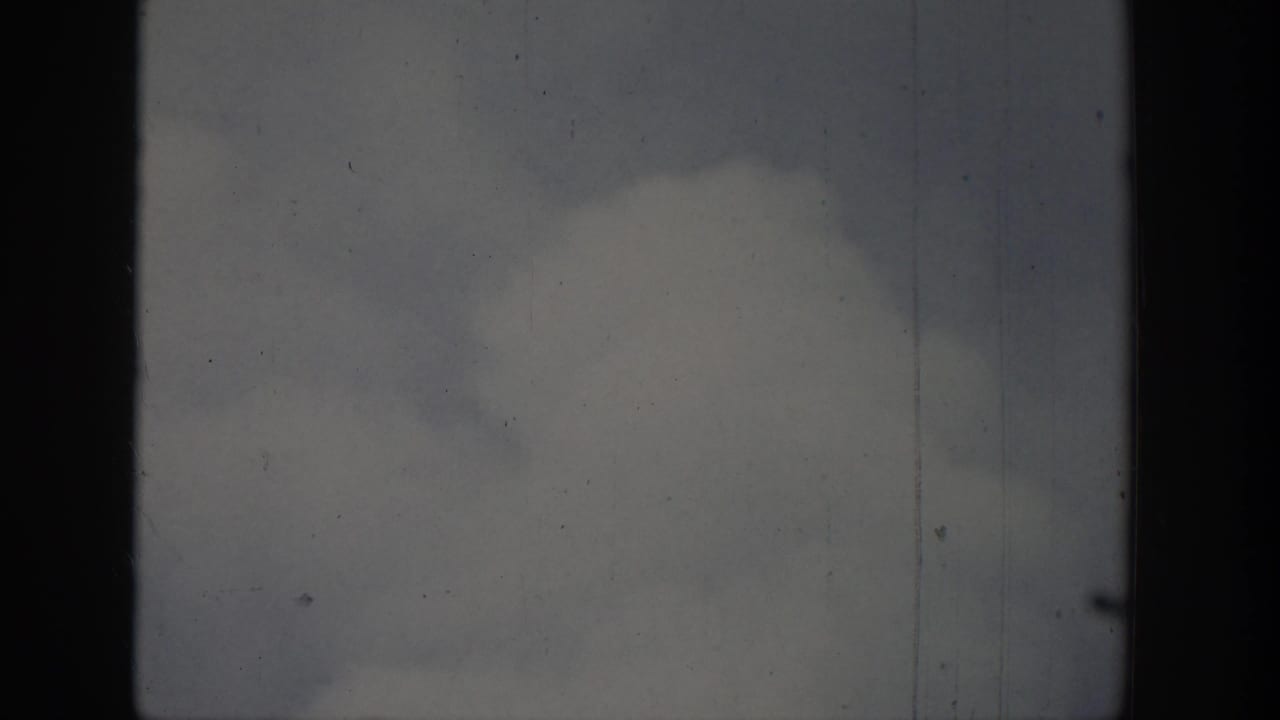 Soft clouds over water with dark vertical framing and film scratches.