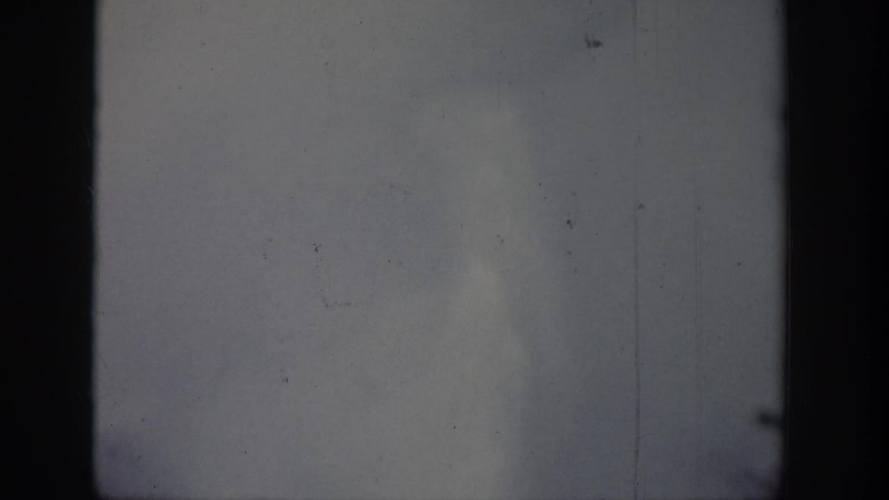 1939 Wyoming-attributed 8mm frame showing a pale vertical plume or steam column beyond dark foreground tree shapes.