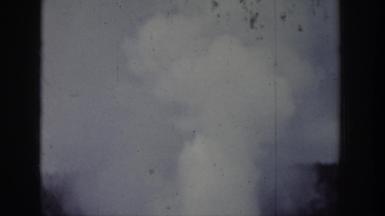 1939 Wyoming 8mm frame showing a geyser plume and steam rising behind dark tree silhouettes.