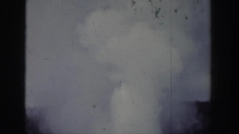 1939 Wyoming 8mm frame showing a geyser plume and steam rising behind dark tree silhouettes.