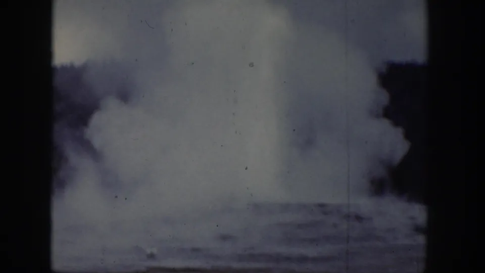 A large geyser steam column in Wyoming, 1939, seen through faded 8mm film with dark trees at the side.