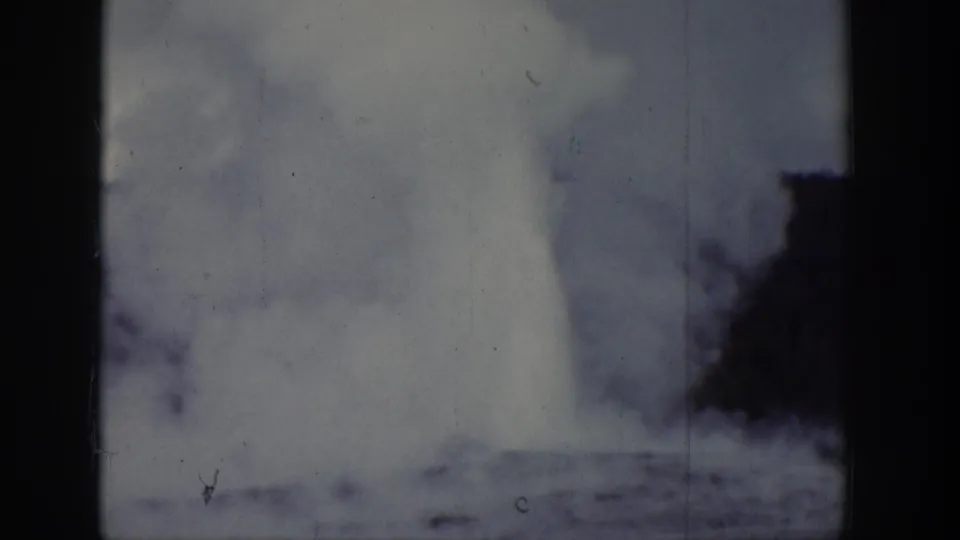 A bright geyser plume rises in a 1939 Wyoming 8mm frame, with steam clouding the view near dark trees.