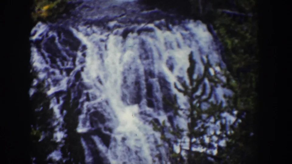 Vintage 8mm frame of the Wyoming waterfall, showing bright cascades against dark stone and surrounding trees.
