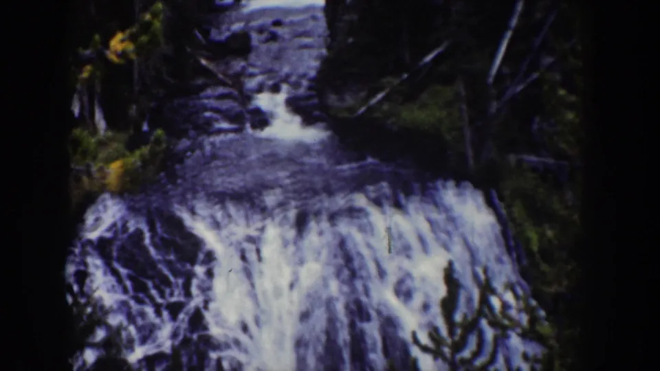 1939 Wyoming home-movie frame with the cascade dropping into a darker stream channel under trees.