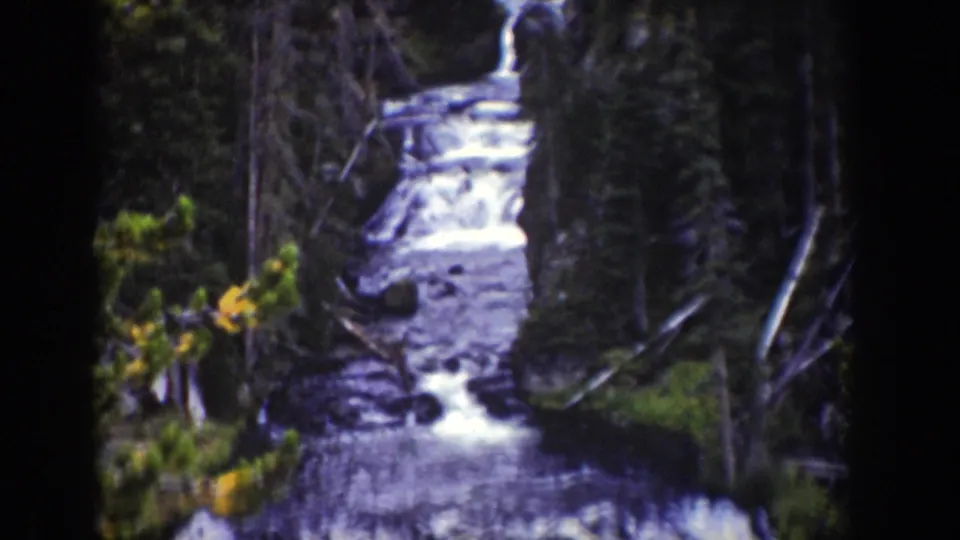 Wider 8mm view of Kepler Cascades in Wyoming, seen through forest with water descending over stepped rock shelves.
