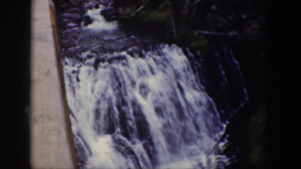 1939 Wyoming 8mm frame showing rushing stream water over rocks in a forested valley.