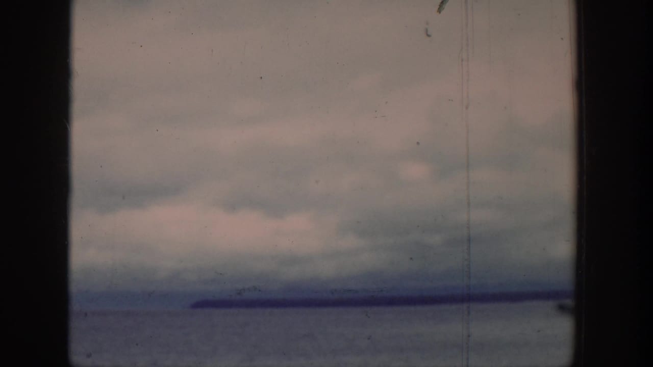 Calm lake beneath an overcast sky with distant land on the horizon.