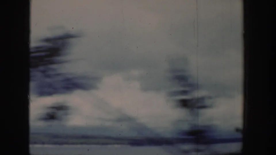 Motion-blurred lakeshore view from the 1939 Wyoming home movie, with water, cloudy sky, and dark tree shapes passing the frame.