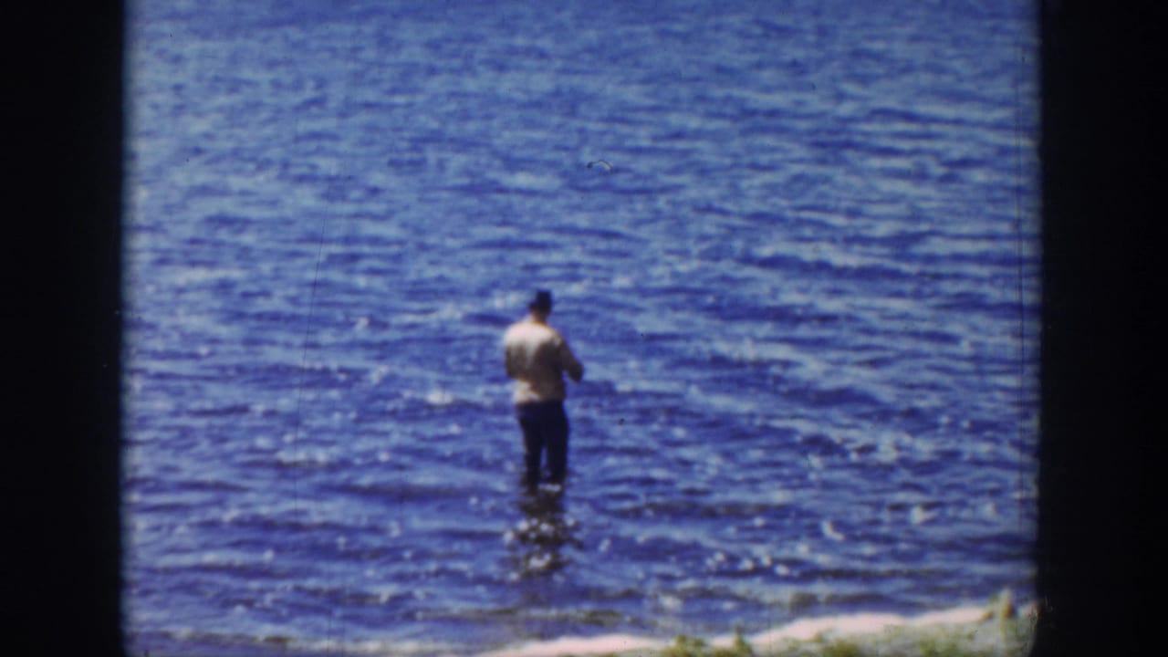 Man stands in blue lake water with his back to the camera.
