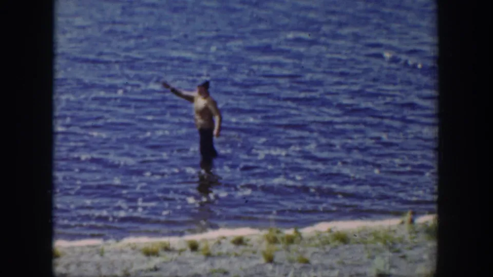 A fisherman in a light shirt casts or raises a rod while standing in a Wyoming lake in 1939 home-movie footage.