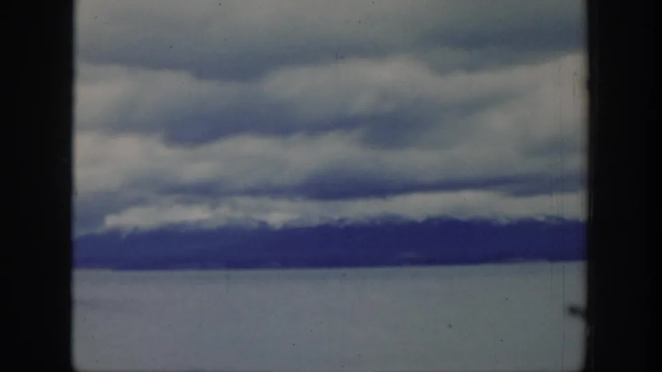 Clouds hang over a lake and dark mountain shoreline in the closing 1939 Wyoming landscape view.