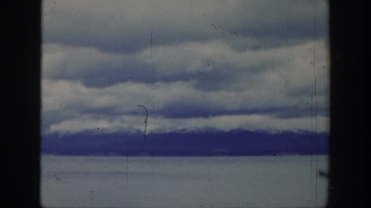 1939 Wyoming home-movie frame showing layered clouds above a distant mountain range, with film gate edges and visible surface wear.