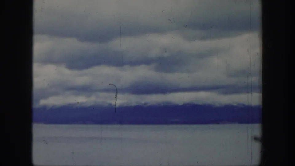 1939 Wyoming home-movie frame showing layered clouds above a distant mountain range, with film gate edges and visible surface wear.