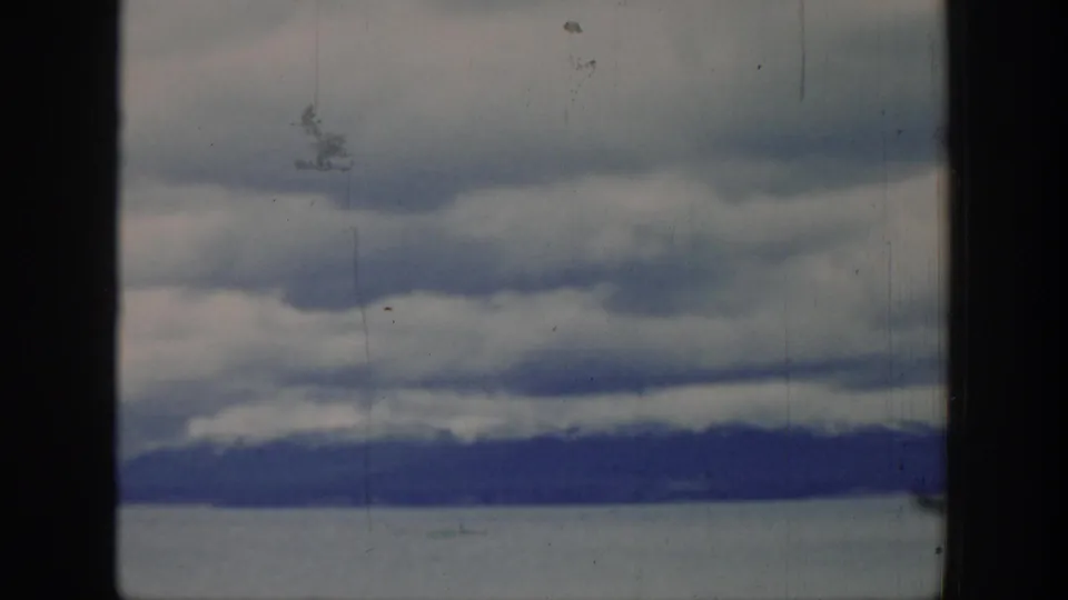 Wyoming landscape frame from the 1939 home movie, showing a dark mountain line beneath layered gray clouds and a pale open foreground.