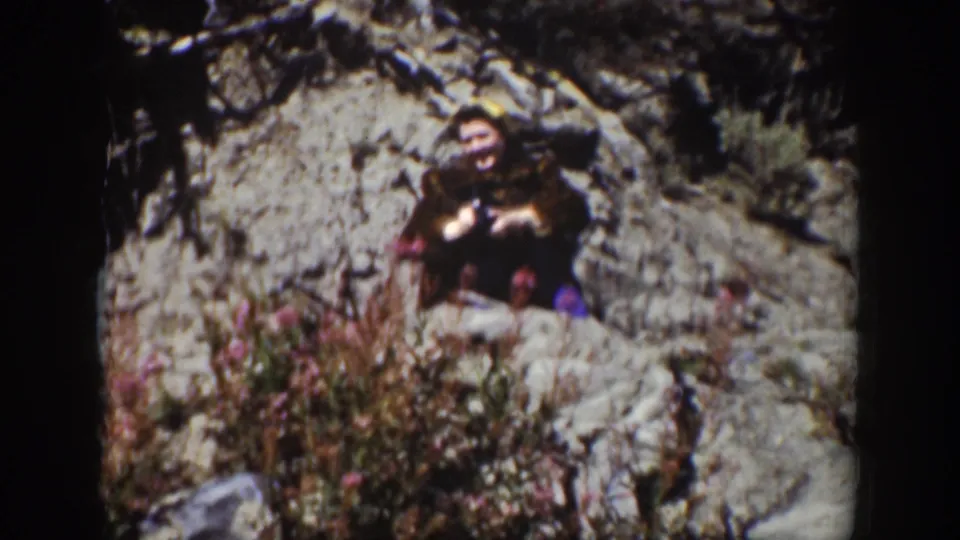 1939 Wyoming 8mm frame showing a person partly obscured among rocks and wildflowers beside a rugged outdoor bank.