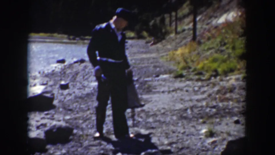 1939 Wyoming 8mm frame showing a man with a bag and stick looking down along a rocky riverside path.
