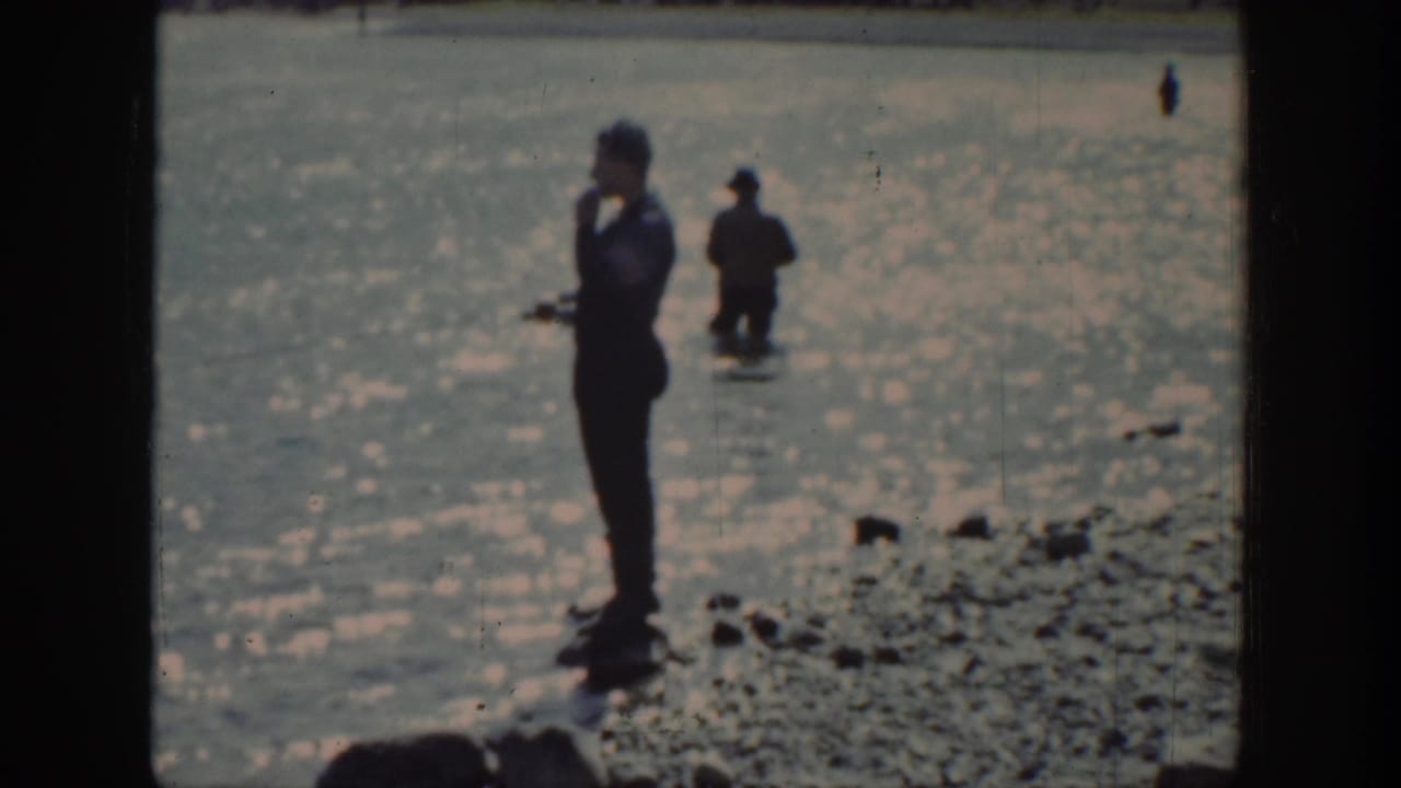 1939 Wyoming home-movie frame showing a man near the rocky lake edge and another person farther out in the water.