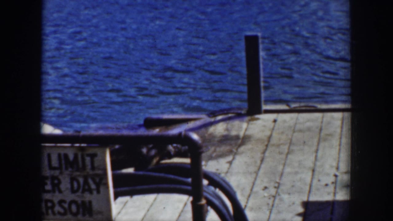 Wooden pier with blue water, railing, vertical posts, and a partial sign.