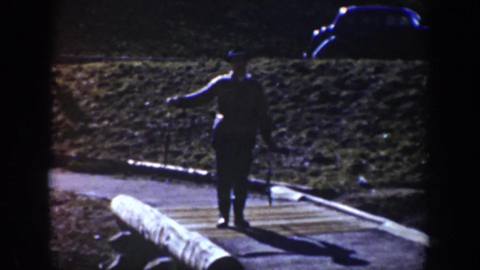 1939 Wyoming 8mm frame showing a distant adult figure on a path with a parked vintage car beyond.
