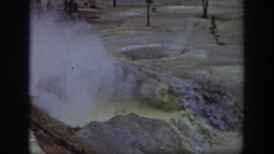 Archival Yellowstone frame of a boiling-looking yellow thermal pool with steam and boardwalk posts beyond.