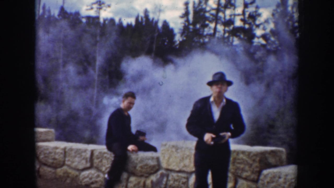 1939 Wyoming home-movie frame showing two adult men by a stone viewing wall as steam rises behind them.
