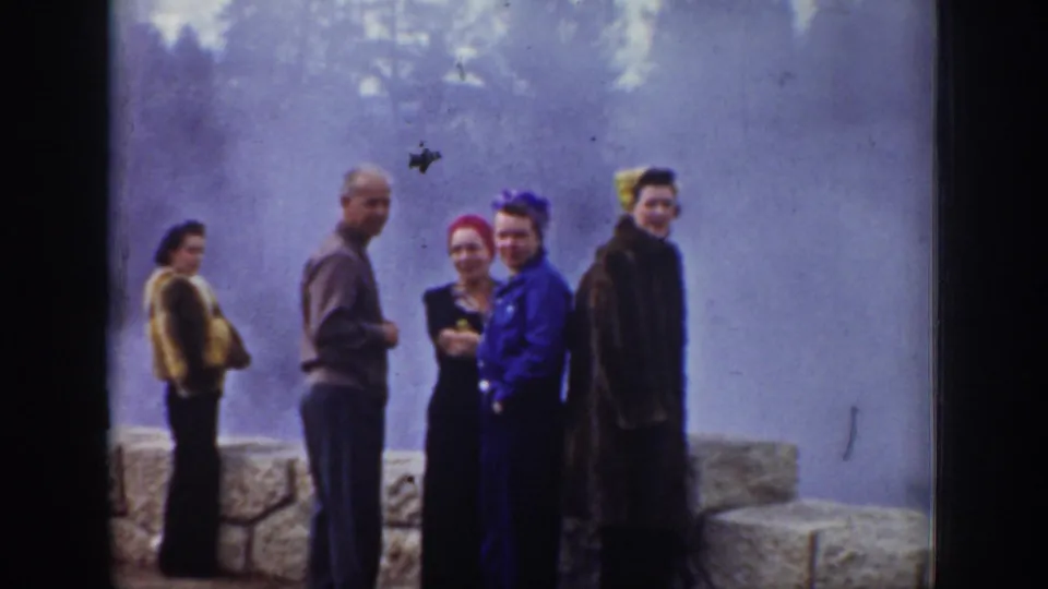Five adult tourists line up near a stone wall at a steaming Wyoming geyser area in 1939 home-movie footage.