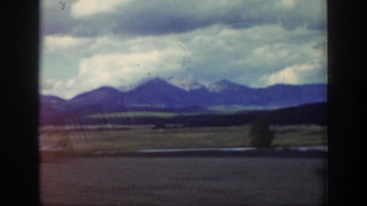 Distant mountain range beyond open valley land, with dark film borders and cloudy sky.