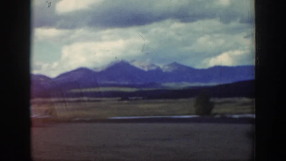 1939 Wyoming home-movie frame with mountain ridges across the horizon, open valley terrain, and a cloudy sky seen through film gate edges.