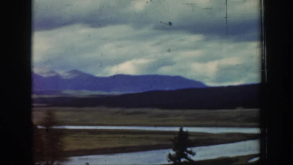1939 Wyoming 8mm view of layered mountain silhouettes, a dark ridge, valley floor, and a pale river or channel under heavy clouds.