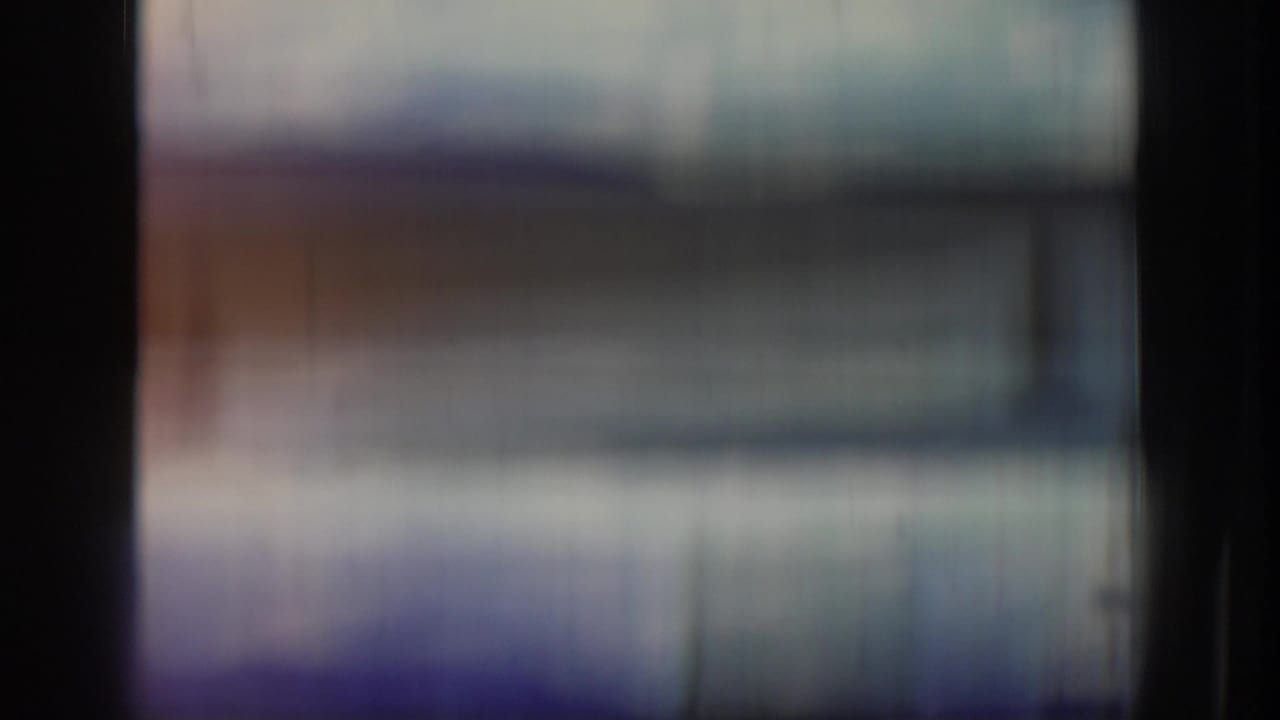 Blurred 8mm contact-sheet frame from the clip opening, with dark frame edges and no clear subjects visible.