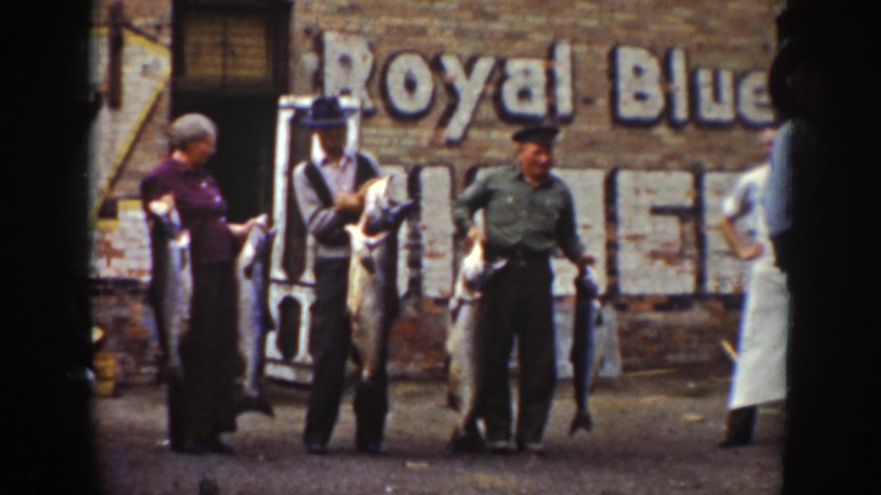 Three adults pose with large fish in front of a brick wall and faded sign.