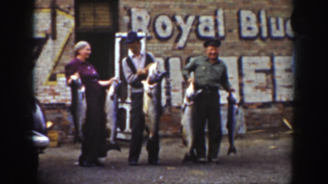 1939 Wyoming home-movie frame of a woman and two men posing with large fish near a brick building marked Royal Blue.