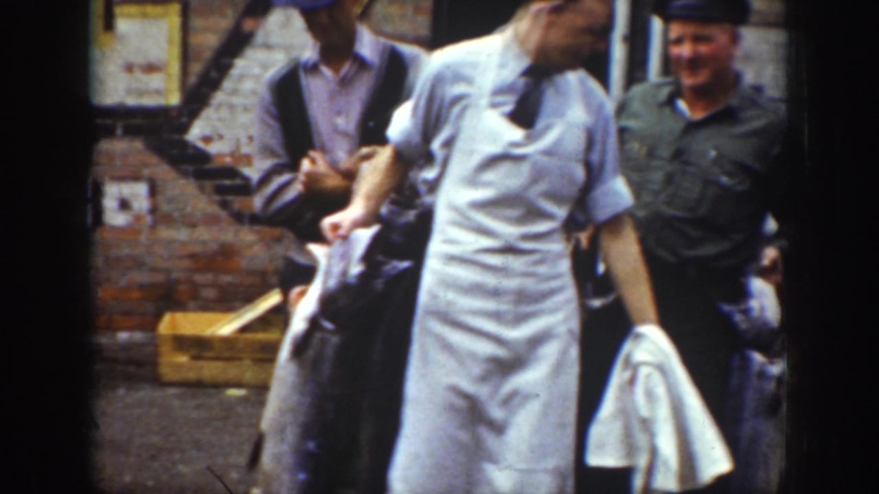 1939 Wyoming home-movie frame showing men in hats near a brick wall, one in white clothing, with large fish being displayed.