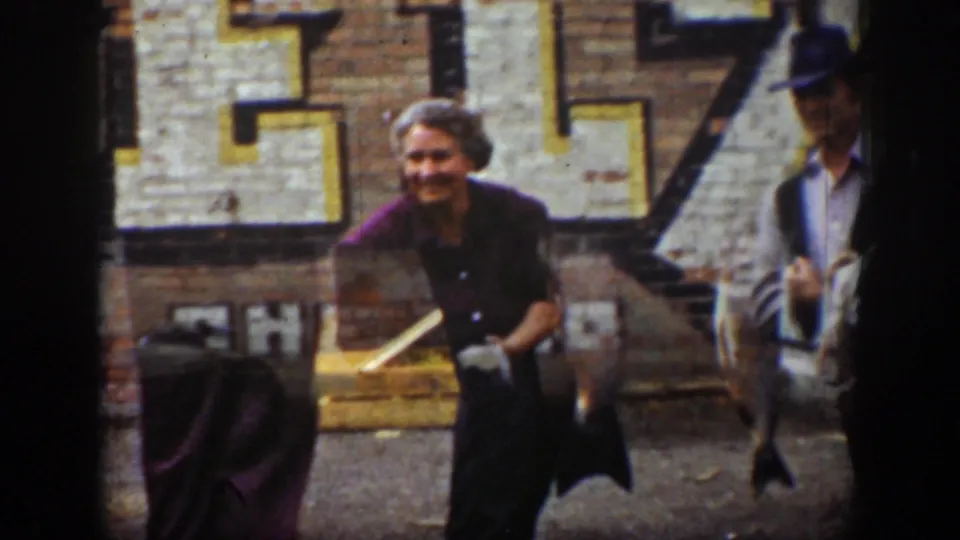 1939 Wyoming frame with a smiling woman holding or standing by large fish in front of a faded Royal Blue sign on a brick wall.