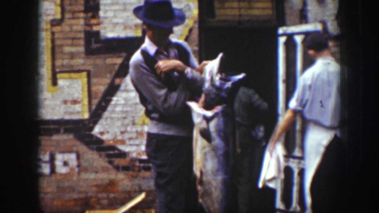 A man in a dark hat holds a large fish while others stand nearby.