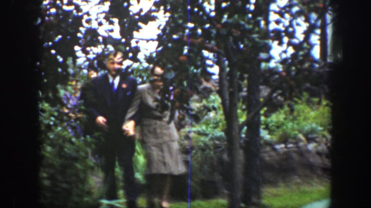 In 1939 Wyoming home-movie footage, a suited man and a woman in a light skirt suit walk together through a garden.