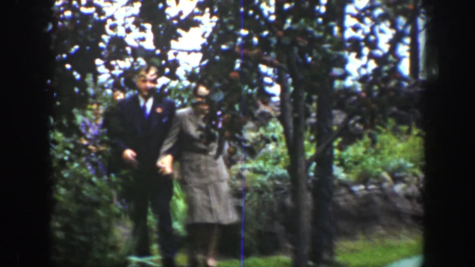 In 1939 Wyoming home-movie footage, a suited man and a woman in a light skirt suit walk together through a garden.