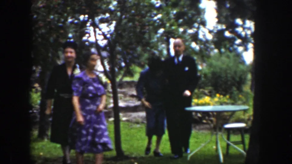 Adults in suits and dresses appear in a Wyoming garden setting, with trees, lawn, yellow flowers, and patio furniture visible.