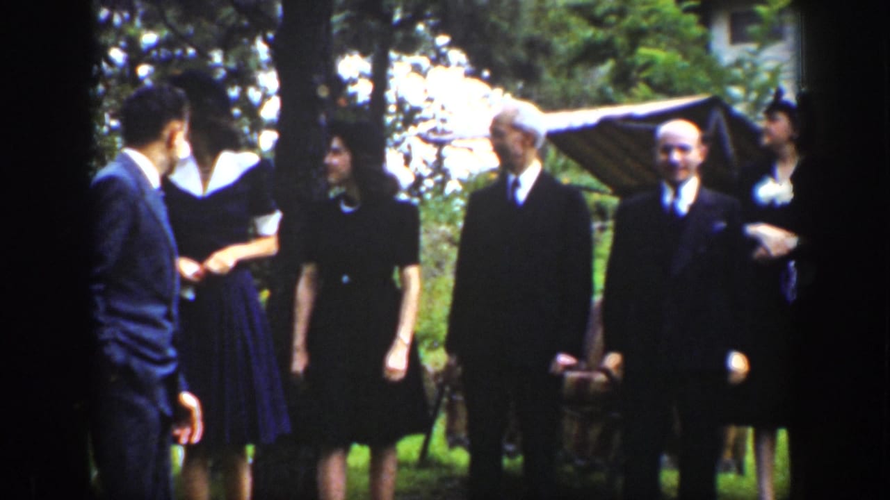 In 1939 Wyoming home-movie footage, adults in suits, dresses, and hats gather outdoors on a grassy yard near trees.