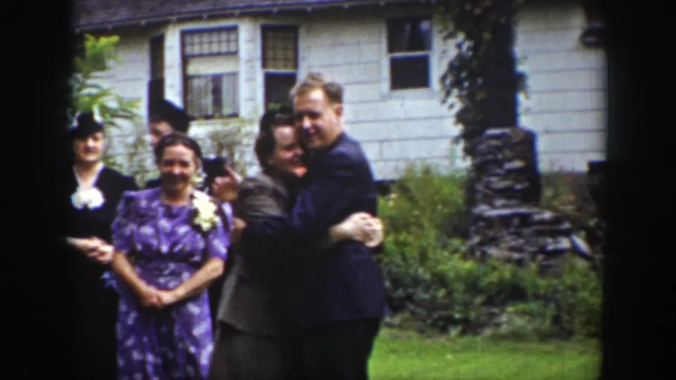 1939 Wyoming wedding home-movie frame with a couple embracing on the lawn while other adults stand near the house.