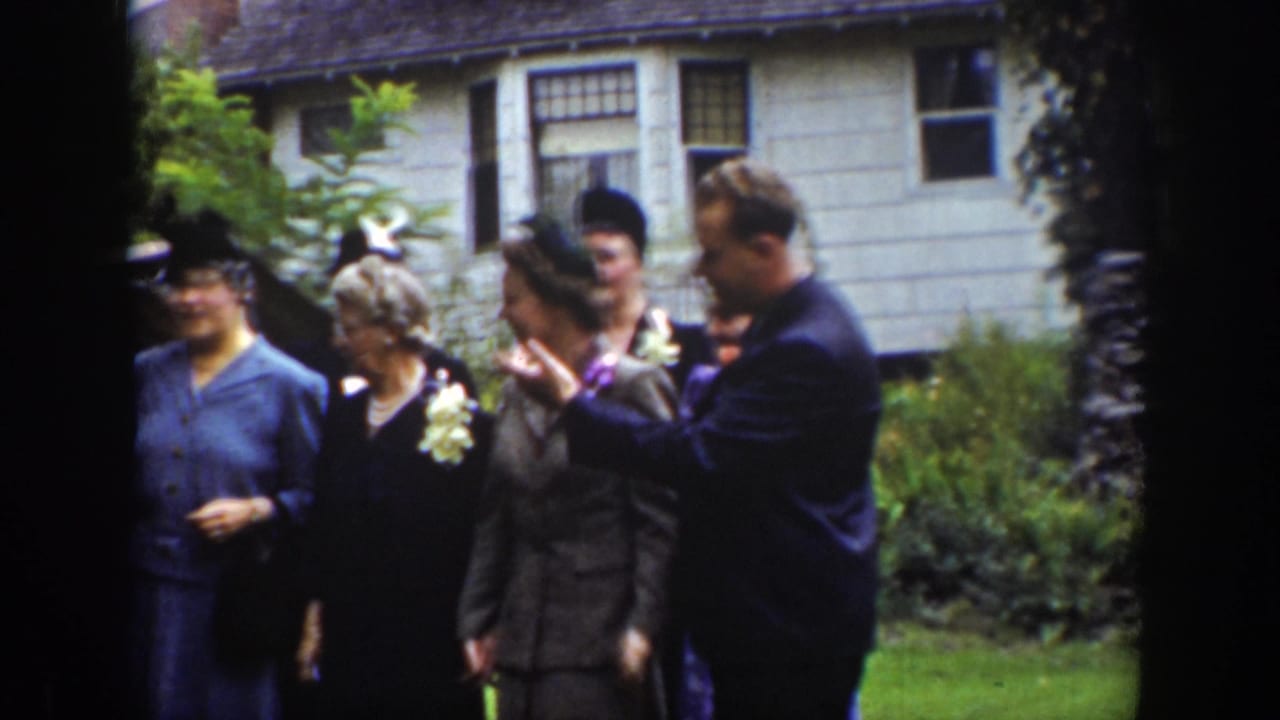 In Wyoming archival 8mm footage from 1939, adults in suits, dresses, hats, and corsages gather outside a house.