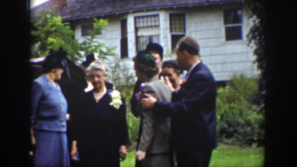 A group of adults in 1939 Wyoming home-movie footage stands in a garden while a man places an arm around another person.