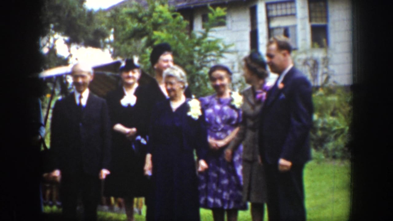 Wyoming 1939 home-movie frame showing adults in suits, hats, corsages, and dresses gathered outdoors near a house.
