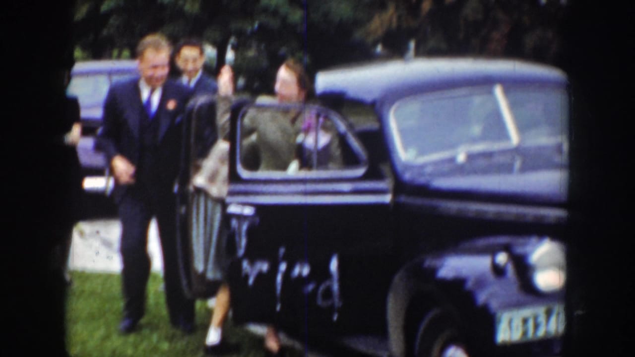 A woman steps into a dark sedan while men in suits stand nearby.