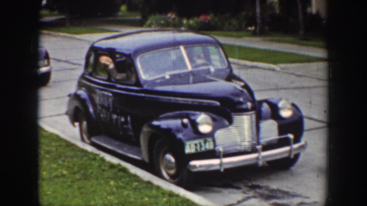 A dark prewar sedan sits along a Wyoming residential street, with a passenger visible through the rear side window.